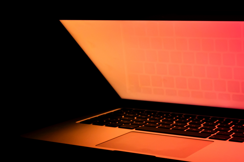 a half-open laptop with a red-orange glow from the screen shining on the keyboard in a dark room